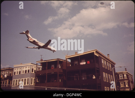 Questa fotografia cattura un aereo in arrivo per un atterraggio vicino all'aeroporto Logan, sorvolando l'incrocio tra Frankfort Street e Lovell Street a Boston, Massachusetts. La scena riflette la natura frenetica dell'aeroporto e dei suoi dintorni. Foto Stock