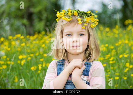 Ragazza che indossa una corona di fiori sulla sua testa, seduto su un prato di fiori, ritratto Foto Stock