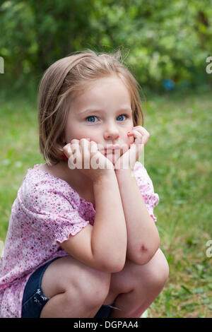 Ragazza, 4, in una posizione accovacciata con un look pensieroso Foto Stock