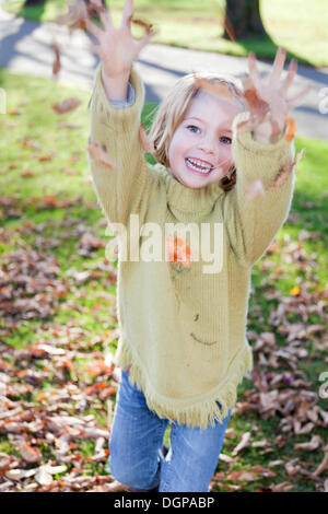 Ragazza, 6, gettando le foglie in autunno Foto Stock