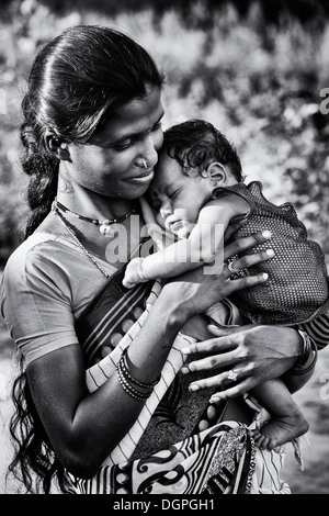 Felice di casta inferiore donna indiana cullano il suo bambino. Andhra Pradesh, India . Monocromatico Foto Stock