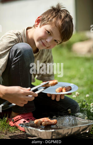 Ragazzo con salsicce su una piastra e un barbecue monouso Foto Stock