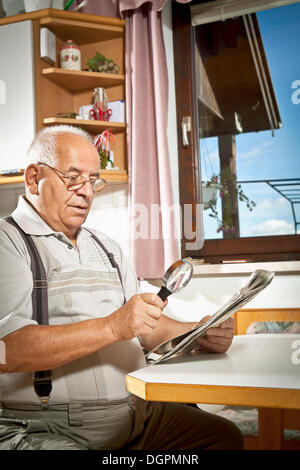 Uomo anziano leggendo un giornale con una lente di ingrandimento Foto Stock