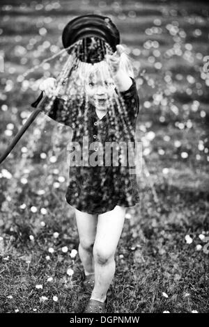 Giovane ragazzo giocando con un tubo flessibile di irrigazione in un giardino Foto Stock