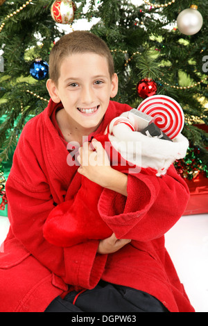 Carino piccolo ragazzo aprendo la sua calza di Natale di fronte all'albero. Foto Stock