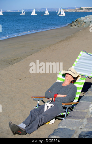 La donna si rilassa sulla sedia spiaggia sulla spiaggia di San Francisco Foto Stock