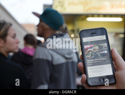 Berlino, Germania. 22 ottobre, 2013. Una donna può contenere uno smartphone visualizzare le app del sito web di viaggio "TripAdvisor', che raccomanda il snack bar visibile in background, a Berlino (Germania), 22 ottobre 2013. Foto: BERND VON JUTRCZENKA/dpa/Alamy Live News Foto Stock