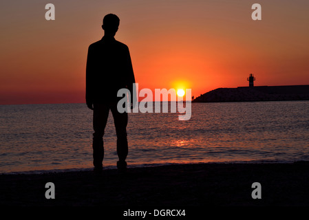 Silhouette di giovani permanente sulla spiaggia al tramonto Foto Stock