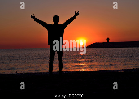 Silhouette di giovani permanente sulla spiaggia al tramonto Foto Stock