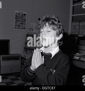 Bambino ragazzo fede cristiana preghiera occhi chiusi tenuta mani in preghiera scuola elementare classe vintage retro nero e bianco immagine foto Llanwrda Carmarthenshshire Galles UK Grande Britiain1988 KATHY DEWITT Foto Stock
