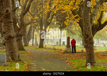 Donna anziana visitando grave nella baia di Ross cimitero in autunno - Victoria, British Columbia, Canada. Foto Stock