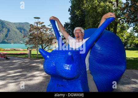 Un uomo fingendo di cavalcare un gigante blu scultura di lumaca. Lugano. Svizzera Foto Stock