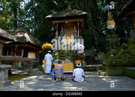 L Induismo di Bali, famiglia di devoti inginocchiati davanti al santuario, bramino sacerdote in tunica bianca, Pura Griya Sakti tempio nei pressi di Ubud, Bali Foto Stock