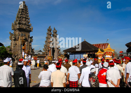 L Induismo Balinese, la raccolta dei credenti, cerimonia, credenti in costumi bianchi tempio portante un santuario d'oro, la torre del tempio Foto Stock