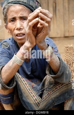 Vecchia donna della Mouchi gruppo etnico seduto sul pavimento con le mani giunte, indossando indossati abiti tradizionali e hat, la povertà Foto Stock