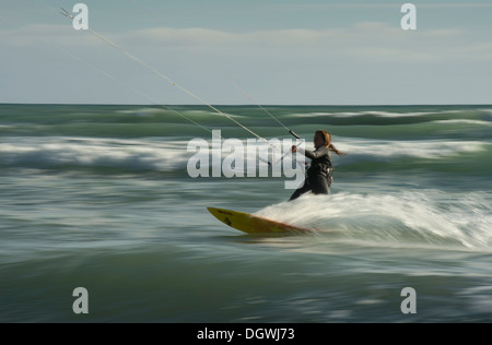 Femmina kitesurfer cavalcando le onde, panning shot Foto Stock