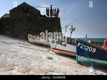 Barche da pesca in uno scalo a Sennen Cove, Cornwall, con reti essiccamento in background Foto Stock