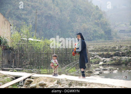 Nero tribù hmong donna fare il bucato con un bambino helper in Cat Cat Village, vicino a Sapa in Vietnam Foto Stock