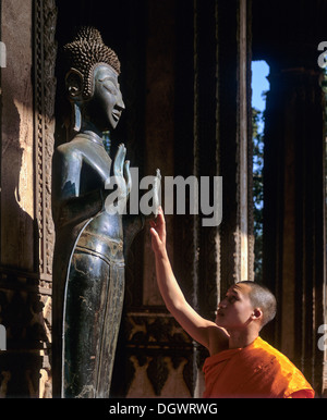 Monaco toccando una statua del Buddha, altare del Buddha di Smeraldo, Wat Ho Prakeo, Ho Phra Keo tempio, Museo Nazionale, Vientiane Foto Stock