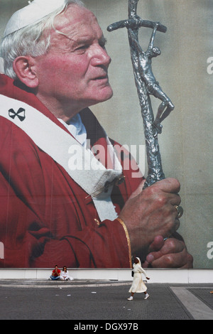 Due turisti che si siedono di fronte a un enorme poster del Papa Giovanni Paolo II, nun a piedi nella parte anteriore del poster, Vatikanstadt, Italia Foto Stock
