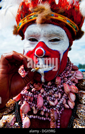 Uomo in un colorato costume decorato con vernice faccia fumare una sigaretta nella tradizionale sing-sing raccolta, Hochland Foto Stock