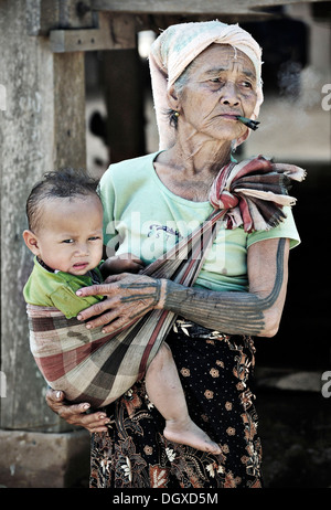 Il fumo la nonna che porta i suoi nipoti in una imbracatura in un villaggio sul Mekong, Laos, Asia sud-orientale, Asia Foto Stock