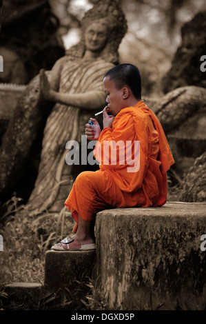 Monaco di fumare una sigaretta in Buddha Park vicino a Vientiane, Laos, Asia sud-orientale, Asia Foto Stock