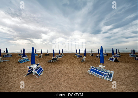 Ripiegata di sedie a sdraio e ombrelloni sulla spiaggia in riva al mare con pioggia nuvole, Cavallino Jesolo Venedig, Italia Foto Stock