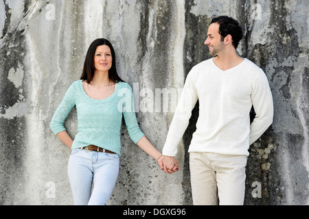 Coppia giovane in piedi mano nella mano di fronte a un muro, Austria Foto Stock