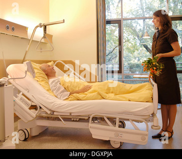 Paziente disteso nel letto di un ospedale è visitato da una donna di fiori di contenimento Foto Stock