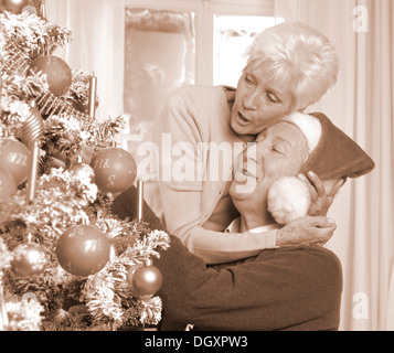 Coppia matura, uomo con un cappello da Babbo Natale, da un albero di Natale Foto Stock