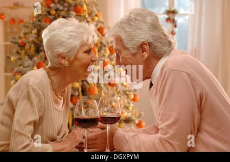 Coppia matura con vino rosso bicchieri seduto davanti a un albero di Natale Foto Stock