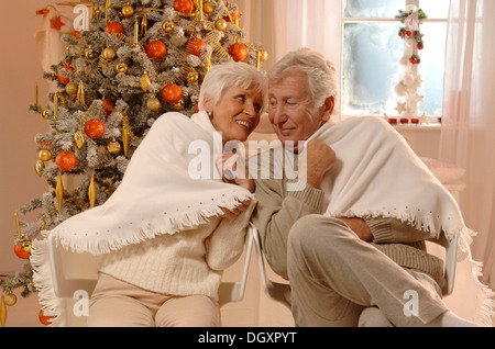 Coppia matura in amore avvolti in un tranciato seduto davanti a un albero di Natale Foto Stock