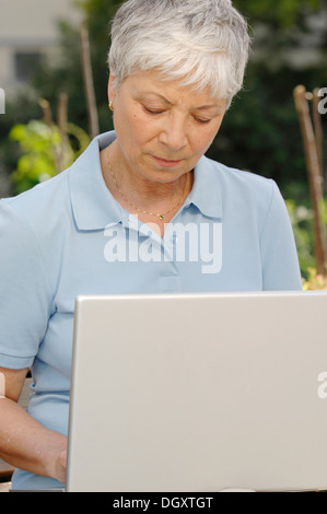 Donna anziana, grigio-pelose, 55-65, lavorando all'aperto su un computer portatile Foto Stock