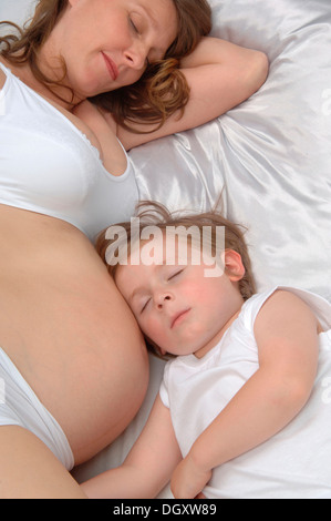 Giovane ragazzo disteso accanto nel ventre di sua madre in stato di gravidanza, sia dormire Foto Stock