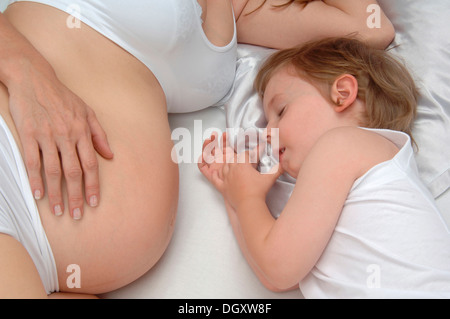 Giovane ragazzo disteso accanto nel ventre di sua madre in stato di gravidanza Foto Stock