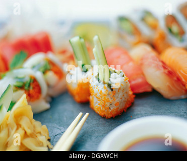 Un assortimento di sushi rotoli con zenzero sott'aceto e bastoncini su una superficie di ardesia Foto Stock