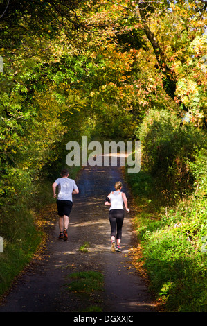 Due pareggiatori per uomo e donna in corsa jogging giù un rurale Somerset lane Foto Stock