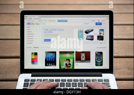 Il sito web di ebay su un MacBook contro una panca in legno sfondo all'aperto tra cui un uomo le dita (solo uso editoriale). Foto Stock