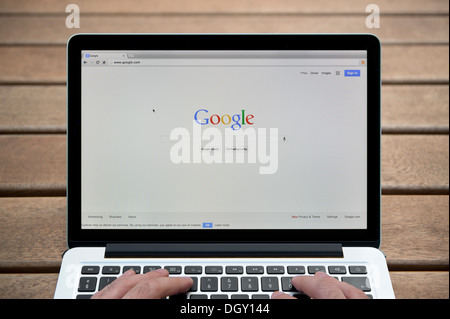 Il sito web di Google su un MacBook contro una panca in legno sfondo all'aperto tra cui un uomo le dita (solo uso editoriale). Foto Stock