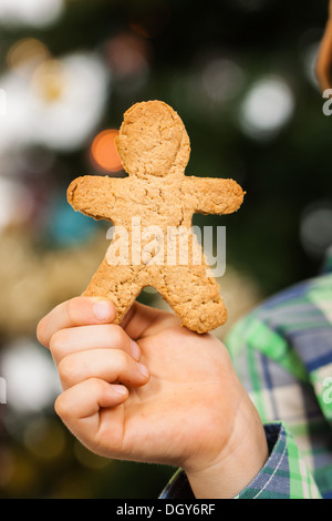 Un bambino la mano è in possesso di un omino di pan di zenzero nella parte anteriore di un albero di Natale. Foto Stock