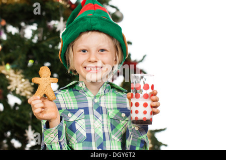 Giovane ragazzo carino che indossa un elf cappello bambino di un albero di Natale tenendo bicchiere di latte e pan di zenzero uomo. Isolato su bianco. Foto Stock