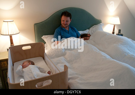 I nuovi genitori in letto, mamma addormentato, papà svegli a guardare la loro bambina Foto Stock