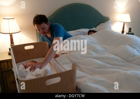 I nuovi genitori in letto, mamma addormentato, papà consolante la sua piccola bambina e tenendo la mano Foto Stock