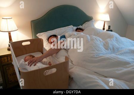 I nuovi genitori in letto, mamma addormentato, papà consolante la sua piccola bambina e tenendo la mano Foto Stock