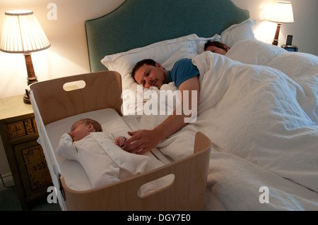 I nuovi genitori in letto, mamma addormentato, papà consolante la sua piccola bambina e tenendo la mano Foto Stock