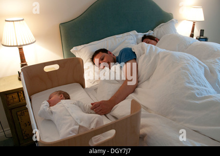 I nuovi genitori in letto, mamma addormentato, papà consolante la sua piccola bambina e tenendo la mano Foto Stock