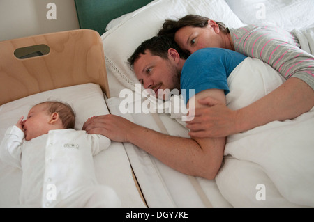 I nuovi genitori nel letto cuddling, sia sveglio con papà consolante la sua piccola bambina e tenendo la mano Foto Stock