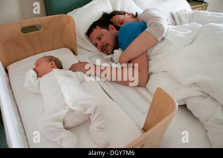 I nuovi genitori nel letto cuddling, papà sveglio consolante la sua piccola bambina e tenendo la mano, mamma addormentato Foto Stock