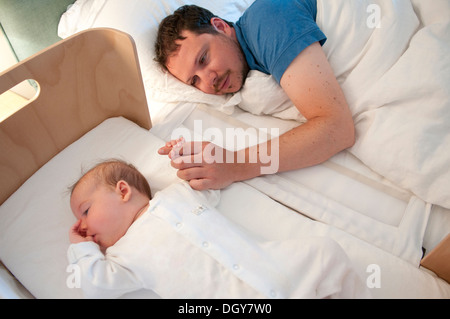 Nuovo padre nel letto consolante la sua piccola bambina e tenendo la mano Foto Stock